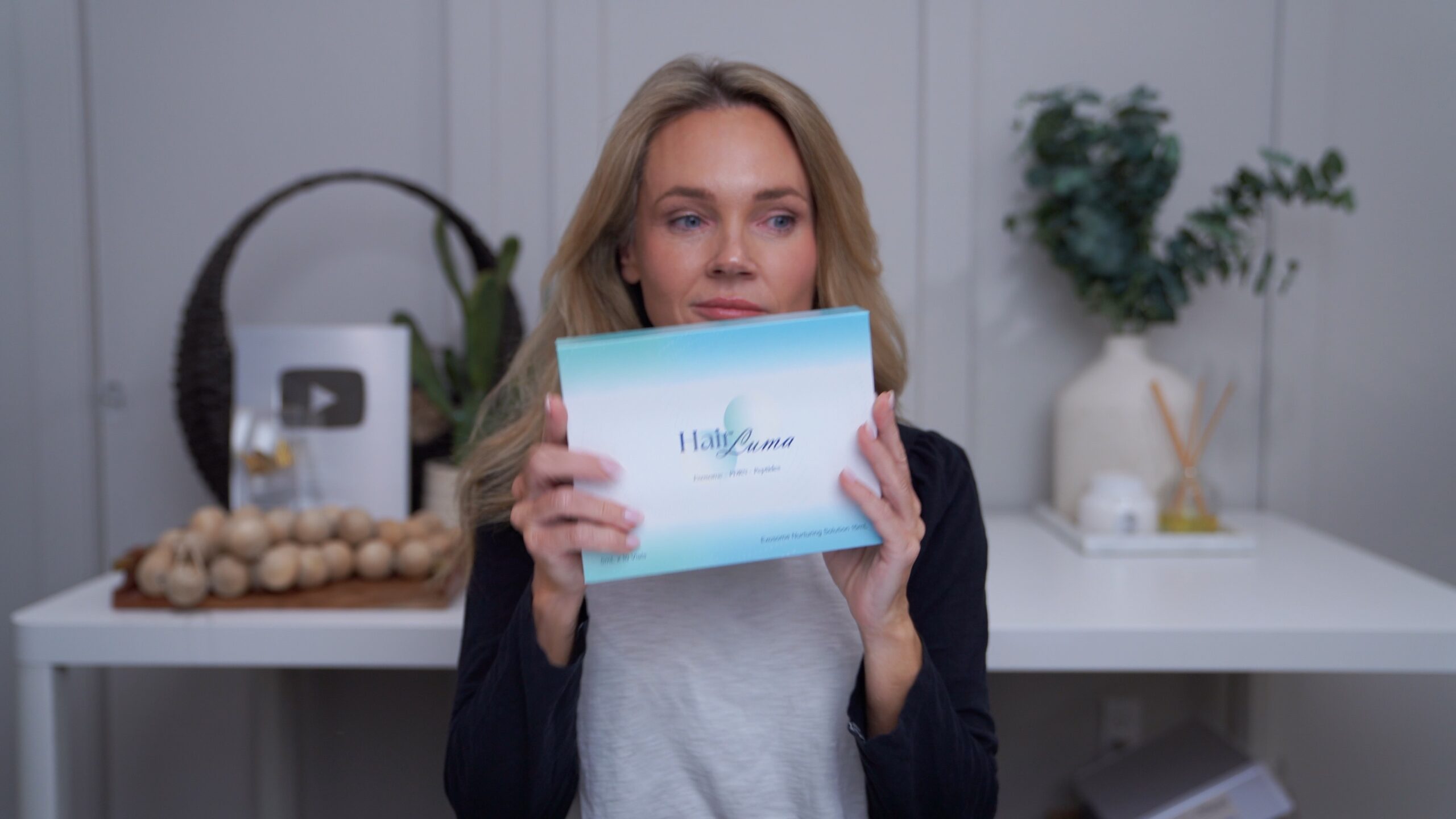 Kim holding the HairLuma scalp system box toward the camera